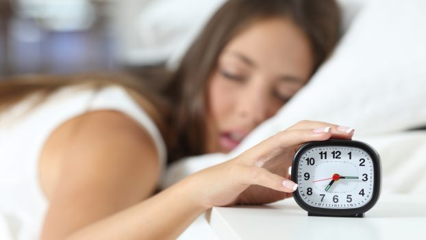 Mujer dormida con un despertador en la mano